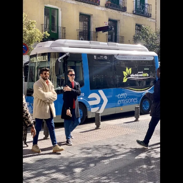 A street photo of a blue city bus with several people walking in front of it